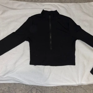 Ribbad långärmad tröja half zip - Svart ribbad långärmad tröja med hög krage och half zip-dragkedja framtill. Tröjan har en slim passform och är perfekt för lager-på-lager. Materialet är stretchigt och bekvämt, vilket gör den enkel att styla till olika outfits. Helt ny