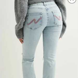 Ljusblå jeans med slitningar från Nelly - Snygga ljusblå jeans från Nelly med bootcut ben och slitna detaljer vid knäna. Jeansen har klassisk femficksdesign, rosa kontrastsömmar och broderade bakfickor. Perfekta för en avslappnad och trendig look.