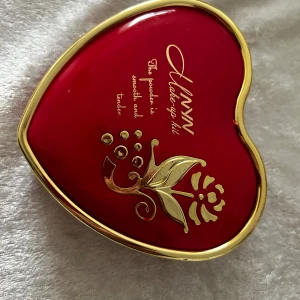 HANNY hjärtformad sminkpalett - Superfin hjärtformad sminkpalett i röd plast med gulddetaljer. Innehåller 10 ögonskuggor i olika färger (rosa, lila, orange, grön, blå, svart, vit, gul, brun, beige), två puder, två rouge, spegel, sminkborste och applikator. Perfekt för dig som gillar färg och kreativitet!