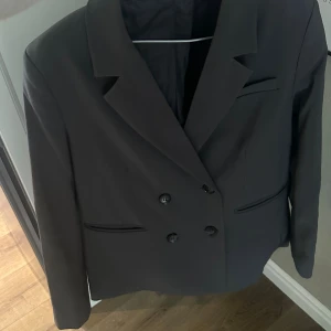 Mörkgrå oversized kavaj NA-KD - Stilren lite oversized mörk grå kavaj från NA-KD med dubbelknäppning och klassisk krage. Kavajen har två fickor framtill och är helfodrad med slät insida. Perfekt för en lite mer uppklädd outfit😇😍