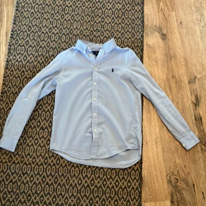 Ljusblå skjorta från Ralph Lauren - Klassisk ljusblå skjorta från Ralph Lauren med broderad logga på bröstet. Storlek 18 vilket motsvarar XS skulle jag säga. Använd tre gånger
