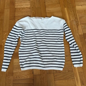 Randig stickad tröja från C'est la vie - Vit och svart randig stickad tröja från C'est la vie. Tröjan har lång ärm, rund hals och är ribbstickad för en skön och avslappnad look. Perfekt för dig som gillar klassisk stil med en twist.