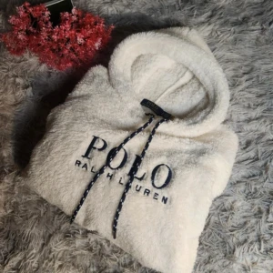 Vit fleece hoodie Polo Ralph Lauren - Supermjuk och fluffig vit hoodie från Polo Ralph Lauren med broderad logga på bröstet. Tröjan har huva med snörning, magficka och långa ärmar. Perfekt för kyliga dagar när du vill vara både bekväm och snygg.
