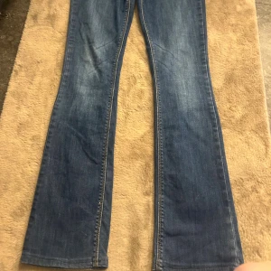 Blå bootcut jeans med klassisk look - Säljer ett par blå jeans med bootcut-modell och klassisk femficksdesign. Jeansen har en snygg tvätt med lätt slitning och raka sömmar. Perfekta för dig som gillar en tidlös stil med lite extra vidd nertill. Materialet är klassisk jeans i bomull.