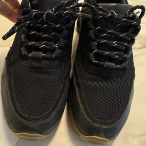 Svarta sneakers Axel Arigato - Säljer ett par svarta sneakers från Axel Arigato med chunky sula i beige och svart. Ovandelen är i mesh och skinn, med svarta snören med vita detaljer. Snygg sportig look och tydlig logga på sidan. Perfekta för dig som gillar streetstyle.