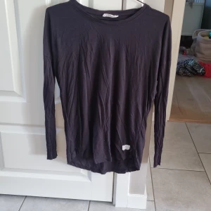 Svart långärmad bomullströja - En enkel svart långärmad tröja i mjuk bomull. Tröjan har rund halsringning och en liten etikett nertill. Perfekt att matcha med jeans eller kjol för en clean look.