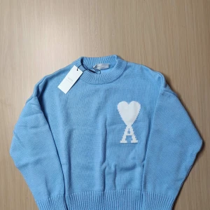 Ljusblå stickad tröja från Ami stl S - Säljer en snygg ljusblå stickad tröja från Ami med ett vitt hjärta och bokstaven A på bröstet. Tröjan har en klassisk rund hals och långa ärmar. Perfekt för en stilren look.