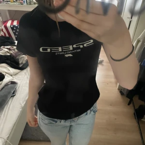 Svart F1 t-shirt med SPEED-tryck - Svart t-shirt från F1 med coolt SPEED WITH NO LIMITS-tryck i vitt på bröstet. Klassisk rund hals och korta ärmar. Skön passform och perfekt för dig som vill ha en skön tränings t-short tröja.