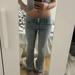 Ljusblå bootcut jeans med låg midja - Säljer ett par ljusblå jeans med bootcut och låg midja. dubbla knappar i midjan och är i stretchigt denimtyg. Snygg passform som sitter tajt upptill och släpper vid vaden. 