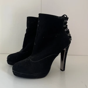 Svarta stövletter med snörning Beauty Girls - Svarta stövletter från Beauty Girls med höga klackar och plattform. Snygga snörningsdetaljer baktill med metallöglor och dragkedja på sidan. Tillverkade i mockaliknande material.