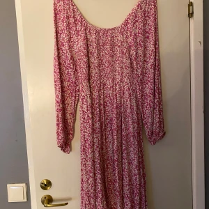 Rosa blommig långklänning med smock - Supersöt långklänning i rosa och vitt med blommigt mönster. Klänningen har smock upptill, långa ärmar med resår vid handlederna och en flowy passform. Perfekt för dig som gillar romantiska vibes och vill sticka ut lite extra.Frakt ingår inte 