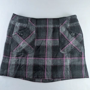 Vintage 90s/Y2K WOOL mini skirt Size 40 from Esprit - Grå och svart rutig kortkjol med rosa detaljer. Kjolen har två framfickor med dekorativa knappar och dragkedja bak. Tjockare tyg med klassisk rutig design, perfekt för en trendig look. Mini skirt with tartan pattern - black, grey and purple  Size 40 (please see label)  Vintage/90s/Y2k  50% wool, 50% viscose  Pockets with buttons  Spare button on label  Lined  Width approx 44cm  Length approx 38cm
