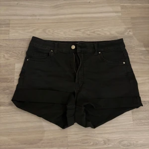 Svarta jeansshorts från H&M - Svarta jeansshorts från H&M i klassisk femficksmodell med uppvikta benslut. Shortsen har bälteshällor, knapp och dragkedja framtill. Perfekta för en chill sommarlook och lätta att matcha med allt.