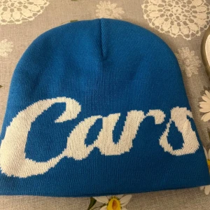  Carlsicko mössa  - Snygg blå mössa från Carlsicko med stor vit text runt hela mössan. Tillverkad i stickad polyester som håller dig varm och ger en cool streetstyle-look. Perfekt accessoar för att sticka ut i mängden under kyliga dagar.