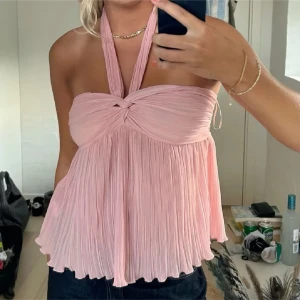 Populär Zara blus - Supersöt plisserad rosa halterneck topp från Zara med twistad detalj framtill. Toppen har en flowy passform och är ärmlös med breda axelband som knyts i nacken. Perfekt för dig som vill ha en luftig och trendig look i sommar.