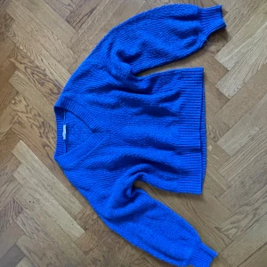 Kornblå stickad tröja Copper Key - Kornblå stickad tröja från Copper Key med v-ringning och breda ribbade muddar vid ärmslut och nederkant. Tröjan har en chunky struktur och lång ärm, perfekt för lager på lager under kyliga dagar.