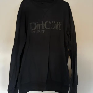 Svart sweatshirt DirtCult San Diego - Svart sweatshirt från DirtCult San Diego med tryckt logga framtill. Använt skick storlek xl men mer en M/L