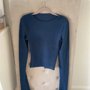 Mörkblå ribbad croppad långärmad topp - Säljer en mörkblå långärmad topp med ribbad struktur och croppad passform. Toppen har en enkel, rund halsringning och rå, ojämn nederkant för en avslappnad vibe. Perfekt att styla med höga jeans eller kjol. Vet tyvärr inte märket💞