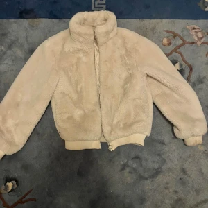 Beige teddyjacka från H&M - Mysig beige teddyjacka från H&M i storlek 164/xxs. Jackan har hög krage, dragkedja framtill och ribbade muddar vid ärmslut och nederkant. Perfekt för kyliga dagar och ger en riktigt soft vibe.
