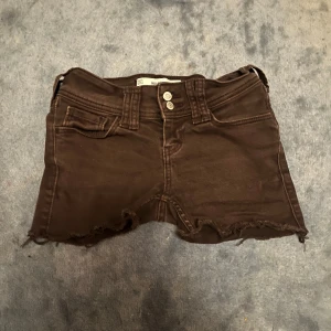 Bruna low-rise shorts från Hollister - Säljer ett par bruna low-rise jeansshorts från Hollister med råa kanter och dubbla knappar framtill. Klassisk femficksmodell med snygga bakfickor och dragkedja. Perfekta för en chill sommarlook. ❗️Dessa shorts var jeans innan men jag gjorde om de till shorts ❗️