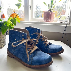 Blå canvas kängor med snörning - Säljer ett par blå kängor i canvas med beige snörning och bruna gummisulor. Skorna har rund tå, synliga vita sömmar. Har lite användning skador därför är priset låg, men skorna kan användas 