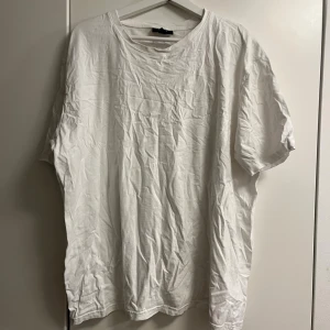 Vit t-shirt från SMOG i XXL - Klassisk vit t-shirt från SMOG i storlek XXL. Modellen är regular fit med rund hals och korta ärmar. Tillverkad i mjuk bomull, perfekt för en clean och enkel stil. Passar dig som gillar en basic look och vill ha en skön t-shirt till vardagen.