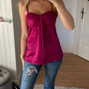 Mörkrosa linnetopp - Säljer en snygg mörkrosa linnetopp med smala axelband och snygg rynkning framtill. Toppen har en lätt glansig finish och är perfekt för dig som gillar en feminin och trendig look. Passar dig som vill ha en enkel men ändå iögonfallande topp.