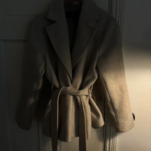 Beige kappa från Vero Moda med bälte - Snygg beige kappa från Vero Moda med klassisk krage och knytskärp i midjan. Jackan har en stilren look och är perfekt för dig som vill ha en enkel men trendig stil. Materialet känns mjukt och jackan har långa ärmar och en rak passform. Den har inte andvänts någon gång bara innomhus. kostar egentligen 700 kr men säljer den för 300, skriv om ni har några frågor!😊