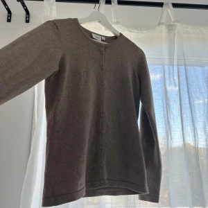 Brun kofta från Saint Tropez - En enkel och stilren brun kofta från Saint Tropez i storlek S. Koftan har rund halsringning, långa ärmar och knäppning med matchande knappar hela vägen framtill. Perfekt att slänga över en t-shirt eller linne när det blir lite kyligt. Tröjan passar äevn Xs och är i nyskick. Använd 2 gånger