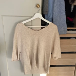 Beige stickad tröja med v-ringning - Snygg beige stickad tröja med v-ringad hals och halvkort ärm. Perfekt för lager-på-lager och passar till både jeans och kjol. Mjuk och skön känsla, enkel att styla för en chill look.