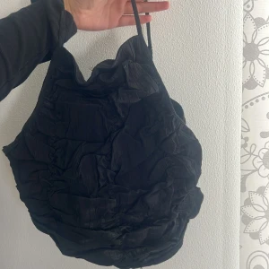 Svart rynkad linnetopp med smala band - Säljer en svart linnetopp med smala, justerbara axelband och rynkad struktur över hela plagget. Toppen har en cool, voluminös look framtill och smockad baksida för skön passform. Perfekt att styla med jeans eller ballong kjol för en trendig vibe.