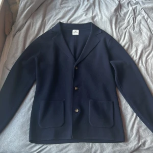 Blå Stickad Blazer Aiden - John Henric - Denna lyxiga kavaj är en perfekt blandning av sofistikering och komfort, tillverkad av en premiumkashmirblandning som ger en mjuk, överseende känsla.  •Flexibel passform •Skarpa slag •Kashmirblandning •Fickor med patch  Material: 90% Ull, 10% Kashmir 