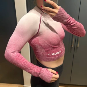 Rosa långärmad croppad topp Gymshark - Säljer en croppad långärmad träningstopp från Gymshark i snygg rosa och vit ombre. Toppen är tight, har tumhål vid ärmsluten och är tillverkad i ett stretchigt syntetmaterial som andas. Perfekt för gymmet eller annan träning. Använd ett fåtal gånger! Som ny 😍