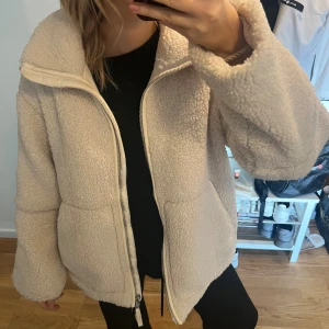  Teddyjacka från H&M - Mysig och oversized teddyjacka i beige med hög krage och hel dragkedja framtill. Jackan har två fickor på sidorna och är tillverkad i fluffigt fleece-material som håller dig varm. Perfekt för kyliga dagar och ger en chill vibe till din outfit. Nyskick 