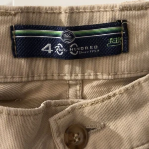 Beiga chinos från Four Hundred - Snygga beiga chinos från Four Hundred med klassisk passform. Byxorna har raka ben, knappstängning och fickor bak med knappdetalj. Tillverkade i bomull för en skön känsla och stilren look. Perfekta för dig som gillar en clean och enkel stil. Ser skrynkliga ut på kamera men skit snygga på säljes då dem blivit för små 