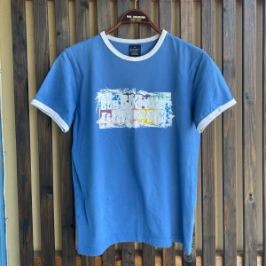 Blå ringer t-shirt  - Blå ringer t-shirt från tdk i storlek XL men en mer sann storlek är M. . Framsidan har ett färgglatt tryck med grafiskt motiv. T-shirten är i mjuk bomull och har en klassisk passform med korta ärmar.