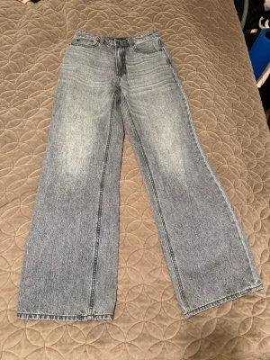 Grå wide jeans från Stradivarius - Säljer ett par grå jeans från Stradivarius i storlek 36. Modellen är wide med hög midja och raka ben, klassisk femficksdesign och knappstängning. Jeansen har en snygg tvättad look och är tillverkade i jeansmaterial.