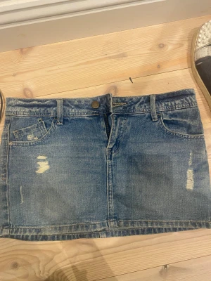Blå jeanskjol från Bershka - Snygg blå jeanskjol från Bershka med klassisk femficksdesign, slitna detaljer och dragkedja framtill. Kjolen är kort och har bälteshällor, perfekt för en avslappnad och trendig look. Materialet är bomull och modellen är rak.