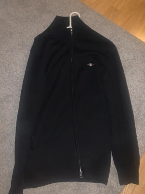 Gant Zip-Kofta - Säljer en helt oanvänd Gant Zip Tröja som jag köpte förra året. Den har aldrig använts och har bara legat i garderoben. Köpt för 1499kr men säljer den för 300kr då jag ändå aldrig kommer använda den oga att det helt enkelt inte är min klädstil. Men den är i toppenskick och väldigt fin.  