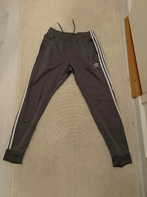 Grå Adidas mjukisbyxor  - Gråa mjukisbyxor från Adidas med klassiska vita ränder. Tröjan till settet finns i min profil. 