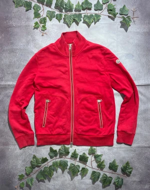 Moncler Maglia Zip Up Röd Sweatshirt Storlek L [ÄKTA] - 🎨 Färg: Röd med vita detaljer 📏 Storlek: Large (L) ♻️ Skick: 9/10 – lättare bruksspår men inga större defekter 🧵 Material: Bomullsblandat sweatshirt-tyg  ✨ Detaljer:         •        Mjuk och bekväm tröjjacka i sweatshirt-material         •        Hög krage         •        Två framfickor med dragkedjor         •        Tvåvägsdragkedja framtill         •        Ribbstickade muddar och midja         •        Moncler-patch på vänster ärm
