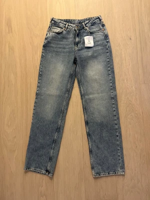  jeans  - Snygga blå Low Wide jeans med låg midja och breda ben. Klassisk femficksmodell i slitstarkt denim med ljus tvätt och subtila slitningar. Perfekt för dig som gillar en avslappnad och trendig look.