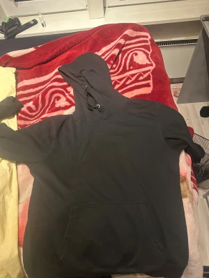 Svart hoodie med ficka och huva - Svart hoodie med klassisk känguruficka framtill och justerbar huva med snörning. Tröjan har långärmade och en enkel, clean design utan tryck eller mönster. Perfekt för dig som gillar en chill och avslappnad stil.