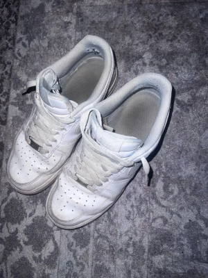 Nike Air Force 1 vita sneakers - Nike Air Force 1 sneakers i helvitt med klassisk låg siluett. Skorna har snörning, perforerad tå och platt sula. 