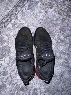 Svarta Nike Air Max 270 sneakers - Nike Air Max 270 sneakers i svart med röda detaljer och synlig Air-enhet i sulan. Ovandelen är stickad mesh för bra ventilation och har snörning. 