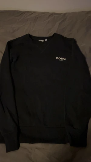 Svart tröja från Björn Borg - Svart långärmad tröja från Björn Borg med enkel och clean design. Liten vit logga på bröstet och rund halsringning. Perfekt för dig som gillar stilrena basplagg. Tillverkad i mjuk bomull för skön känsla.