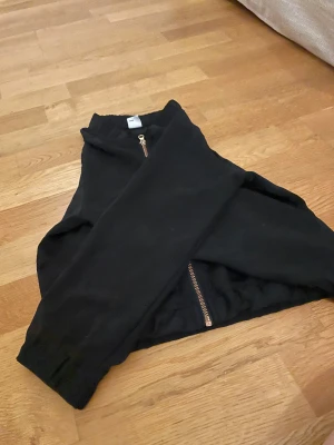 Svart bomberjacka från Lindex - Svart bomberjacka från Lindex med snygg guldfärgad dragkedja framtill. Jackan har långärmade ärmar och ribbade muddar vid ärmslut och nederkant. Perfekt för dig som vill ha en enkel och stilren jacka med coola detaljer.