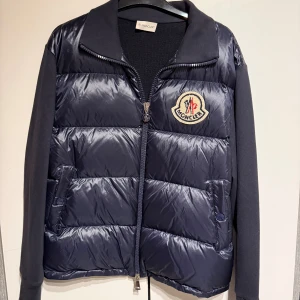 Mörkblå Cardigan från Moncler - Snygg mörkblå cardigan med vadderad front från Moncler med quiltad framsida och mjuka ärmar. Det är en Dam cardigan men passar perfekt på killar också för att den inte är smal i midjan.  Den är köpt förra hösten och är nästan aldrig använd, riktigt bra nu till vintern/hösten. Ny pris - ca 10 000kr , hör av dig för mer info eller bilder! 