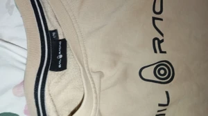 Beige Sail Racing sweatshirt storlek 176 - Snygg beige sweatshirt från Sail Racing i storlek S/M (176). Tröjan har svart logotyptryck på bröstet och en mindre logga nedtill på ryggen. Rund halsringning med svarta ränder på insidan och långa ärmar. Perfekt för dig som gillar stilren streetwear.
