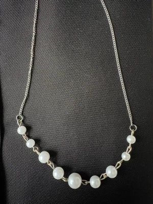 Silverhalsband med vita pärlor - Stilrent halsband med tunn silverkedja och vita pärlor i olika storlekar. Pärlorna är fästa på en rad längs kedjan och ger ett klassiskt och elegant uttryck. Perfekt för dig som gillar enkel men snygg design.